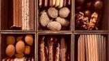 A close-up of an assorted chocolate box divided into six compartments, each holding multiple different types of chocolates: truffles, chocolate-dipped sticks, caramel clusters, and layered bars.
