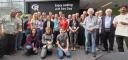 About two dozen R Dev Day participants gathered for a group photo in a bright, glass-walled atrium, in front of a sign reading 'Enjoy coding at R Dev Day'.